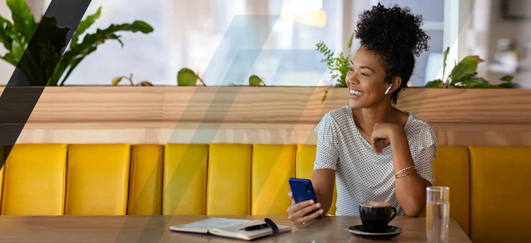 Black woman sitting at a yellow bench seat and smiling. She's holding her phone